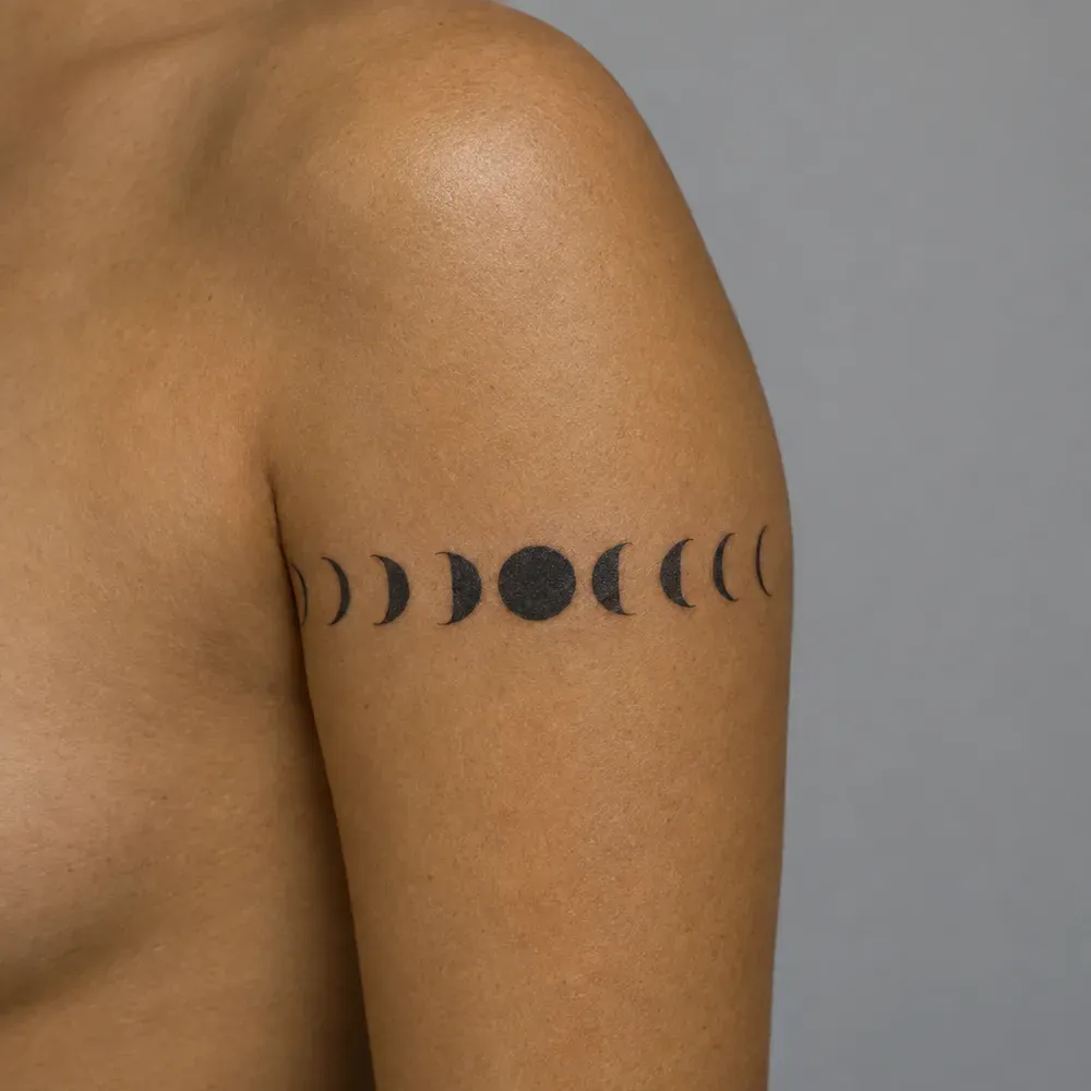 A band of moon phases tattooed around the upper arm, on warm olive skin.