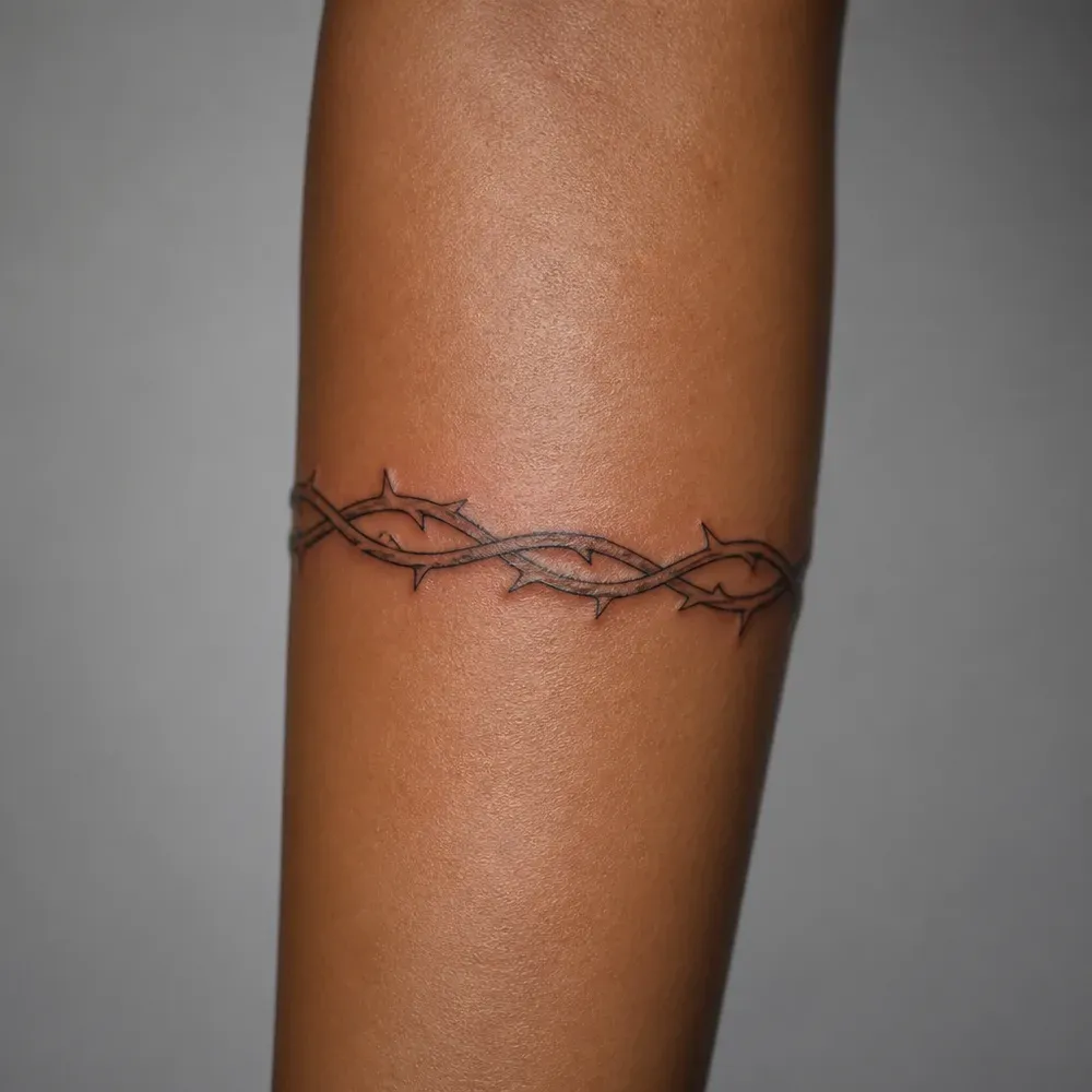 A thorned vine band tattooed around the forearm of warm brown Filipino skin.