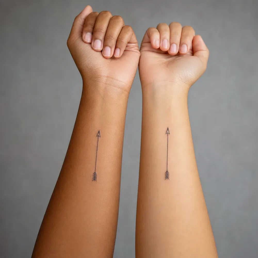 Two slim arrow tattoos, one on each of two people's inner forearms, on warm brown and light tan Filipino skin.