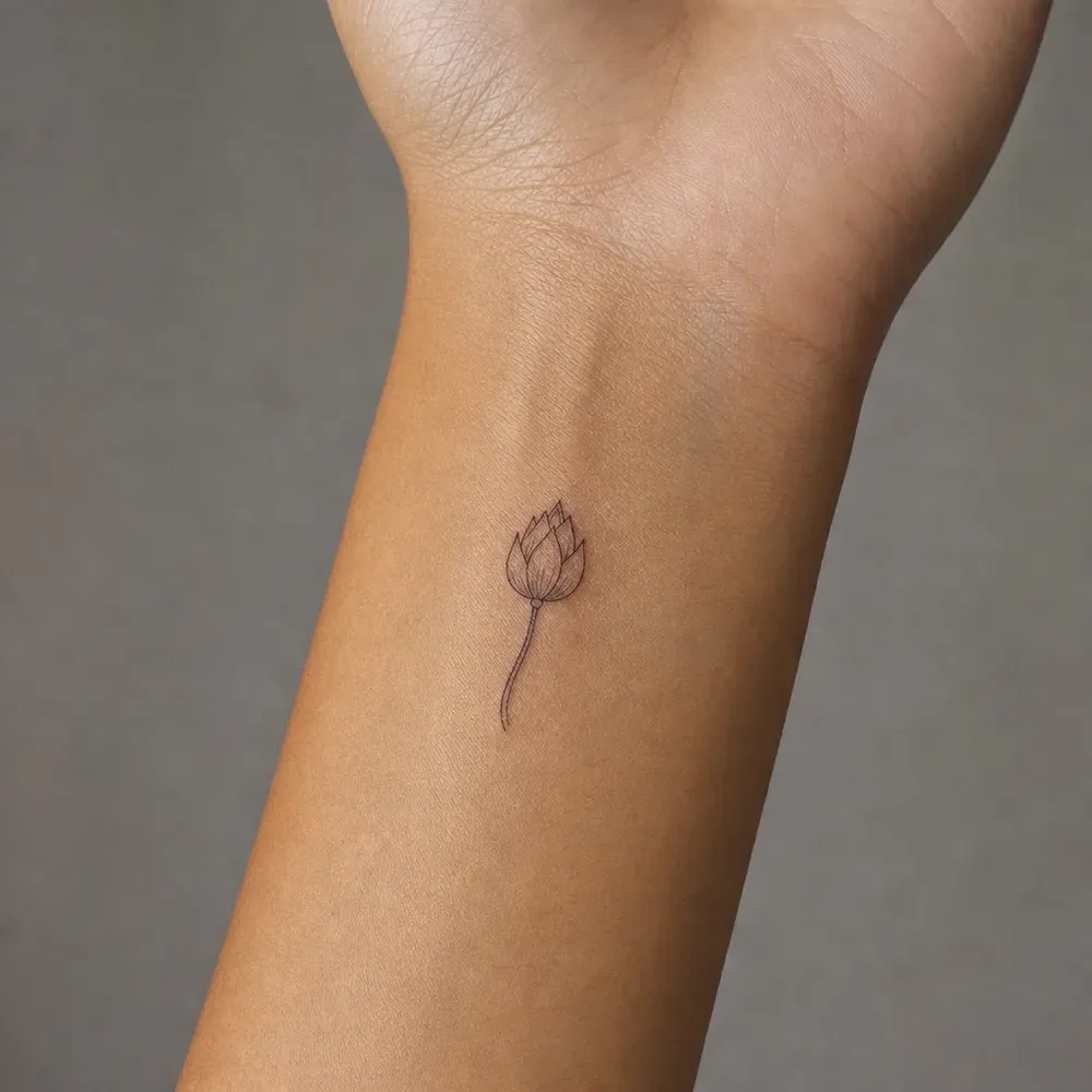A small fine-line closed lotus bud on a thin curved stem, tattooed on the inner wrist of light warm tan skin.