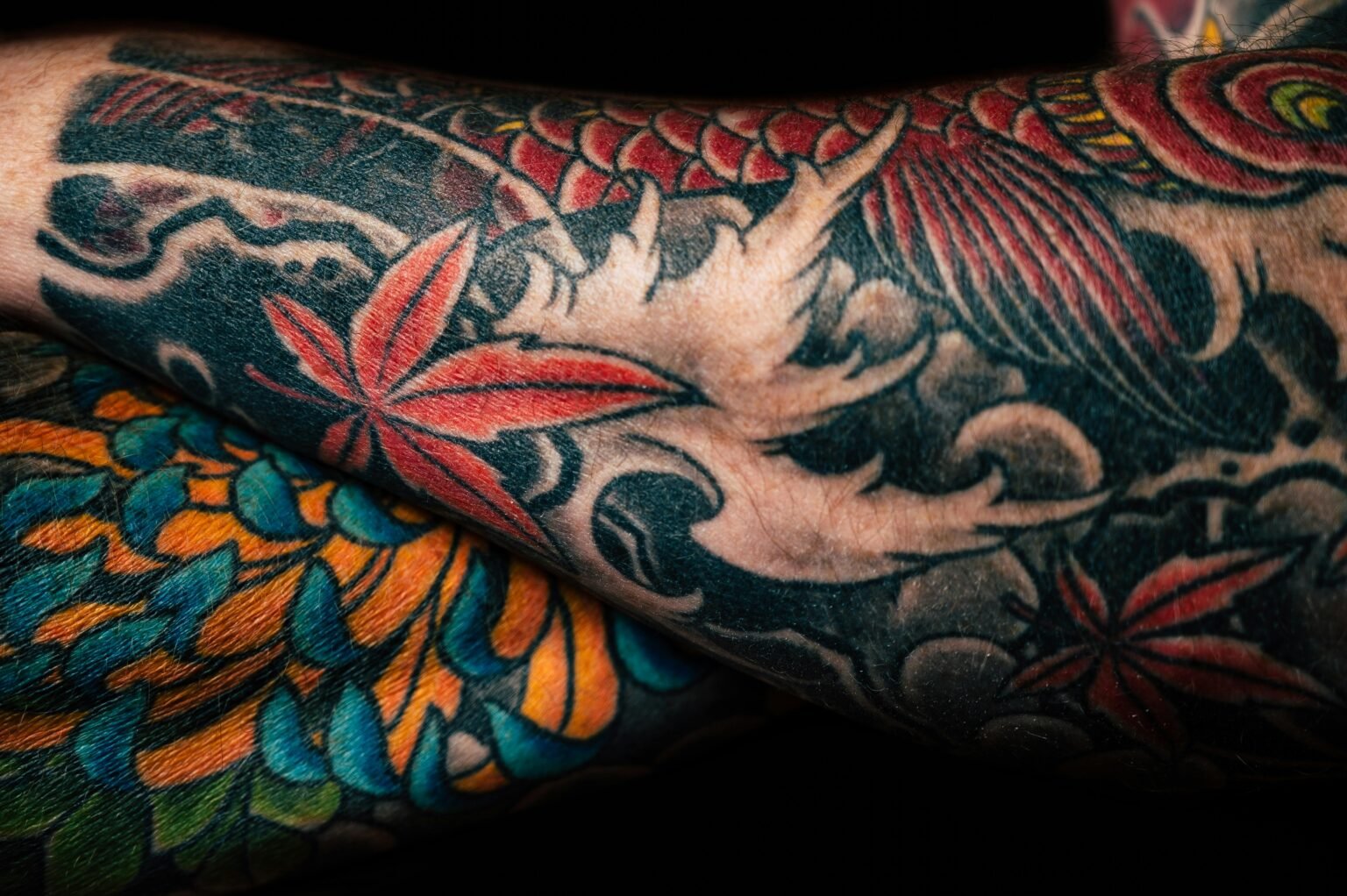 Detailed close-up of colorful sleeve tattoos featuring floral and abstract designs, showcasing artistic creativity.
