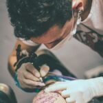 Tattoo artist focuses intently on crafting a detailed leg tattoo in a studio setting.