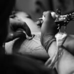 Black and white close-up of a tattoo artist inking a design with precision and focus.